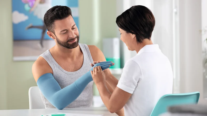 A specialist is checking the fit of a custom-made compression garment glove/sleeve on a patients hand.